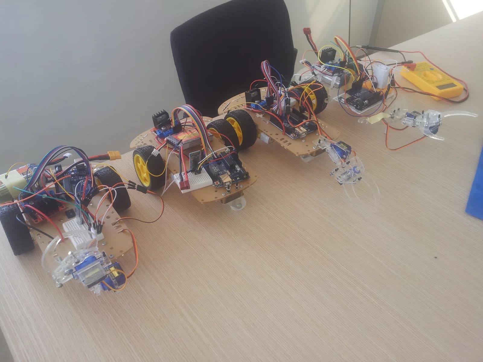 Three hand-built Arduino robots with gripper arms on a workbench during the 2018 robotics internship